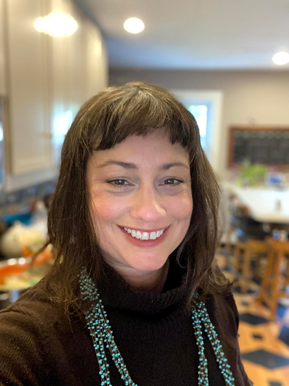 A close-up photo of Rev. Melissa Tustin. She is a white woman with shoulder length brown hair wearing a brown sweater and a necklace made of tiny turquoise beads.